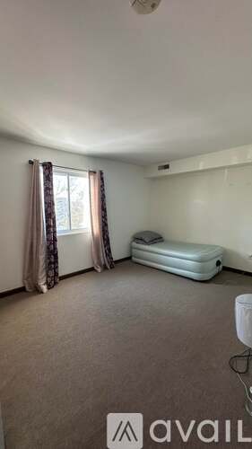 A bedroom with a bed, a window with curtains, and a white air freshener.