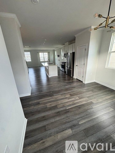 A spacious kitchen with dark wood flooring and white walls.