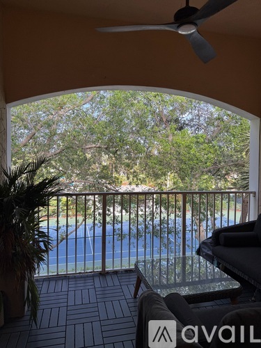 A patio with a table and chairs overlooking a pool and trees.