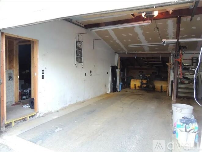 A large empty garage with a door open to a room with a lot of tools.