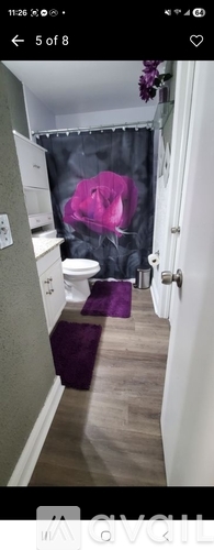 A bathroom with a purple rug and a shower curtain with a pink object on it.