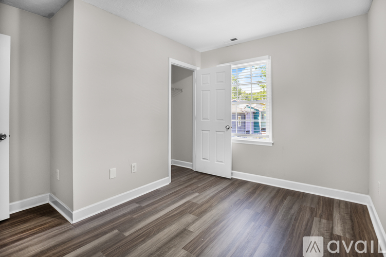 A room with wood flooring and a window showing a view of a pool and trees.