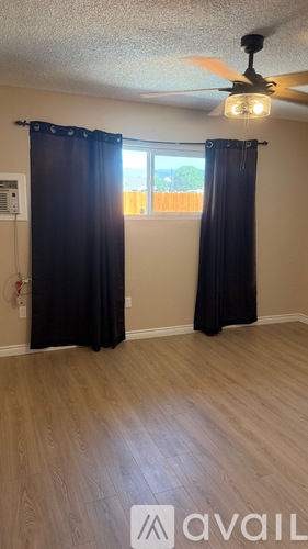 A room with a ceiling fan and a window with black curtains.