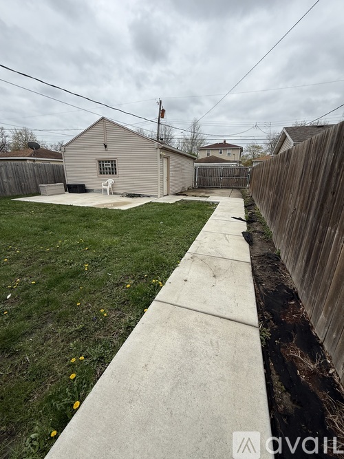 A concrete walkway leads to a small building with a fence on one side.