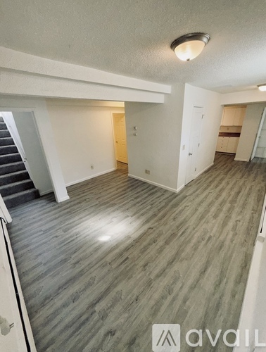 A spacious room with wooden flooring and a staircase on the left side.