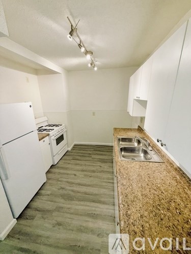 A kitchen with white appliances and a wooden floor.
