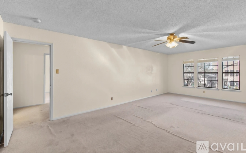 A spacious room with a ceiling fan and a window with bars.