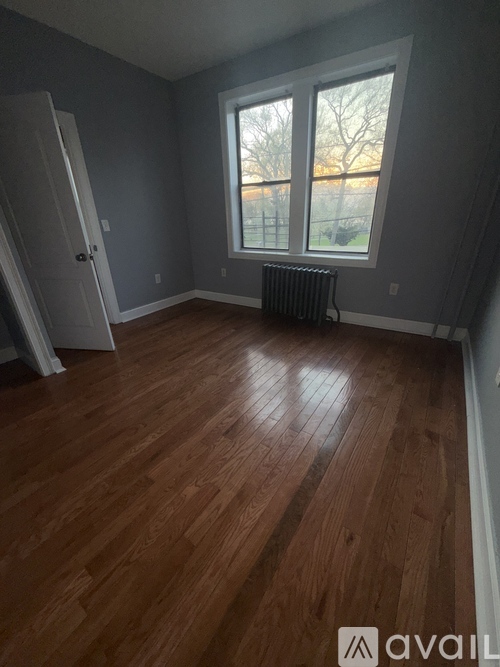 A room with wooden flooring and a window with a view of a fence and trees.