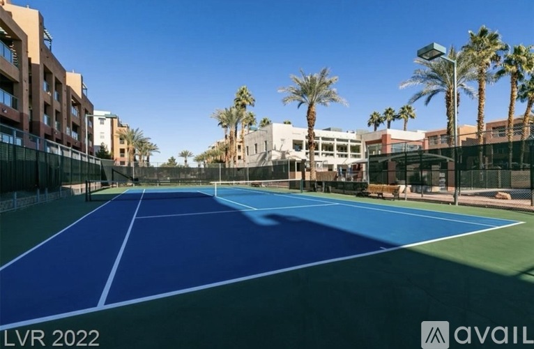 A tennis court is surrounded by buildings and palm trees.