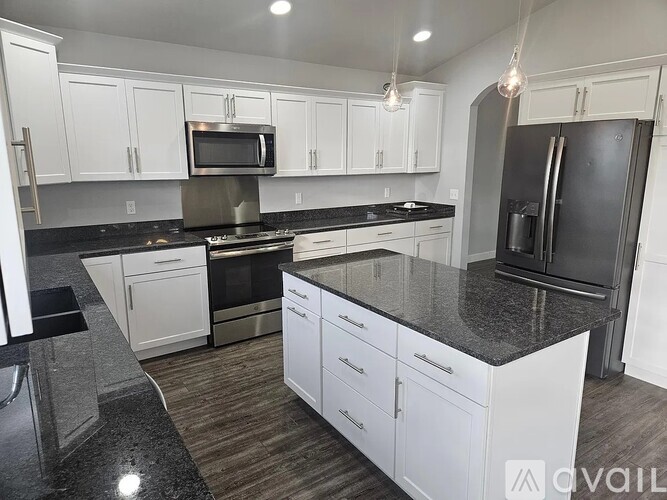 A kitchen with white cabinets and black countertops.