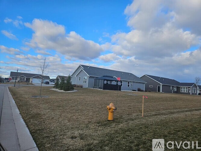 A yellow fire hydrant stands in a grassy field in front of a grey house.