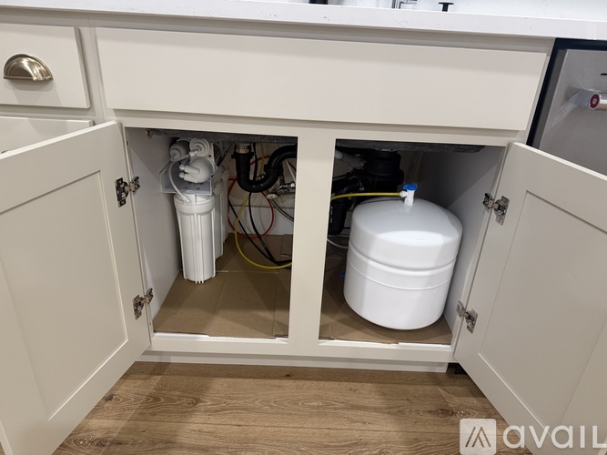A white cabinet with a glass door is open, revealing a white container and some cables.