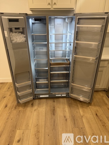A stainless steel refrigerator with its door open, showing the empty shelves and drawers.