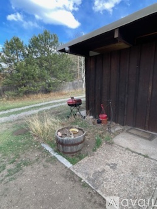 A barn with a red lawnmower and a barrel in front of it.