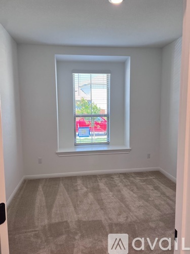 A room with a carpeted floor and a window showing a red car and a building outside.