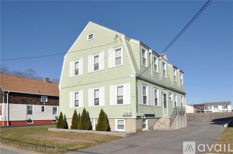 A green two-story building with a white trim and a small front yard with a few trees.
