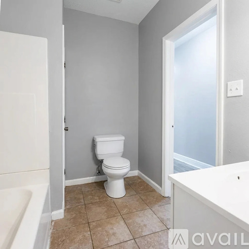 A white toilet sits in a bathroom with a white bathtub.