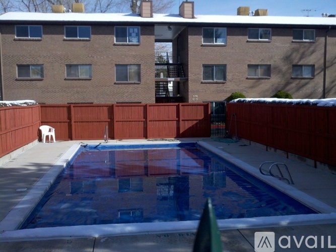 A swimming pool in a backyard with a red fence and a building in the background.