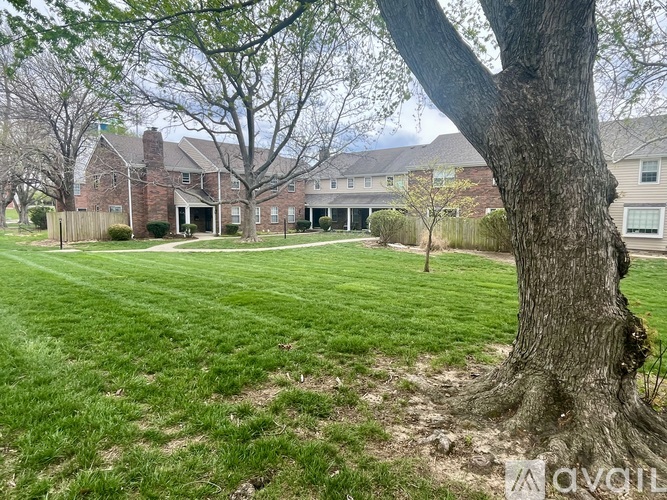 A large tree is in the foreground of a grassy area with a house in the background.