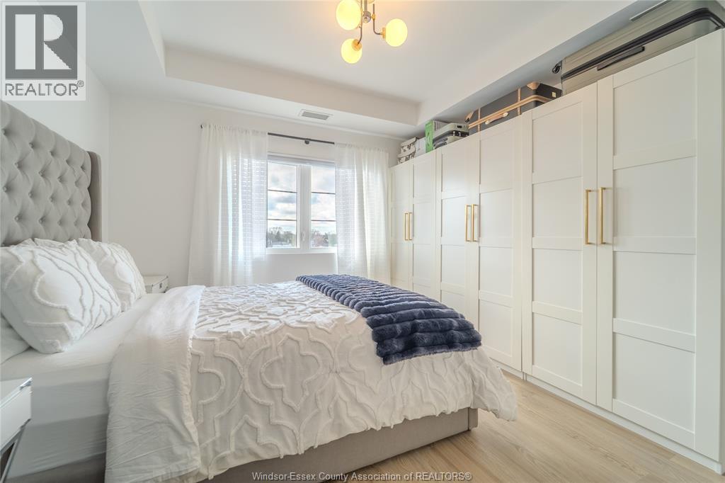 A bedroom with a large bed and a window with white curtains.