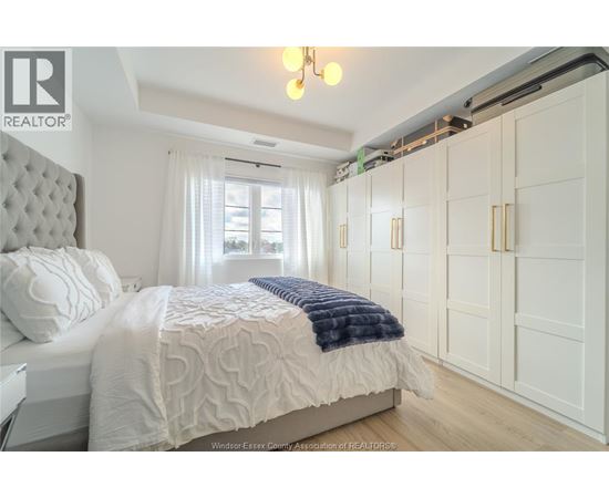A bedroom with a large bed and a window with white curtains.
