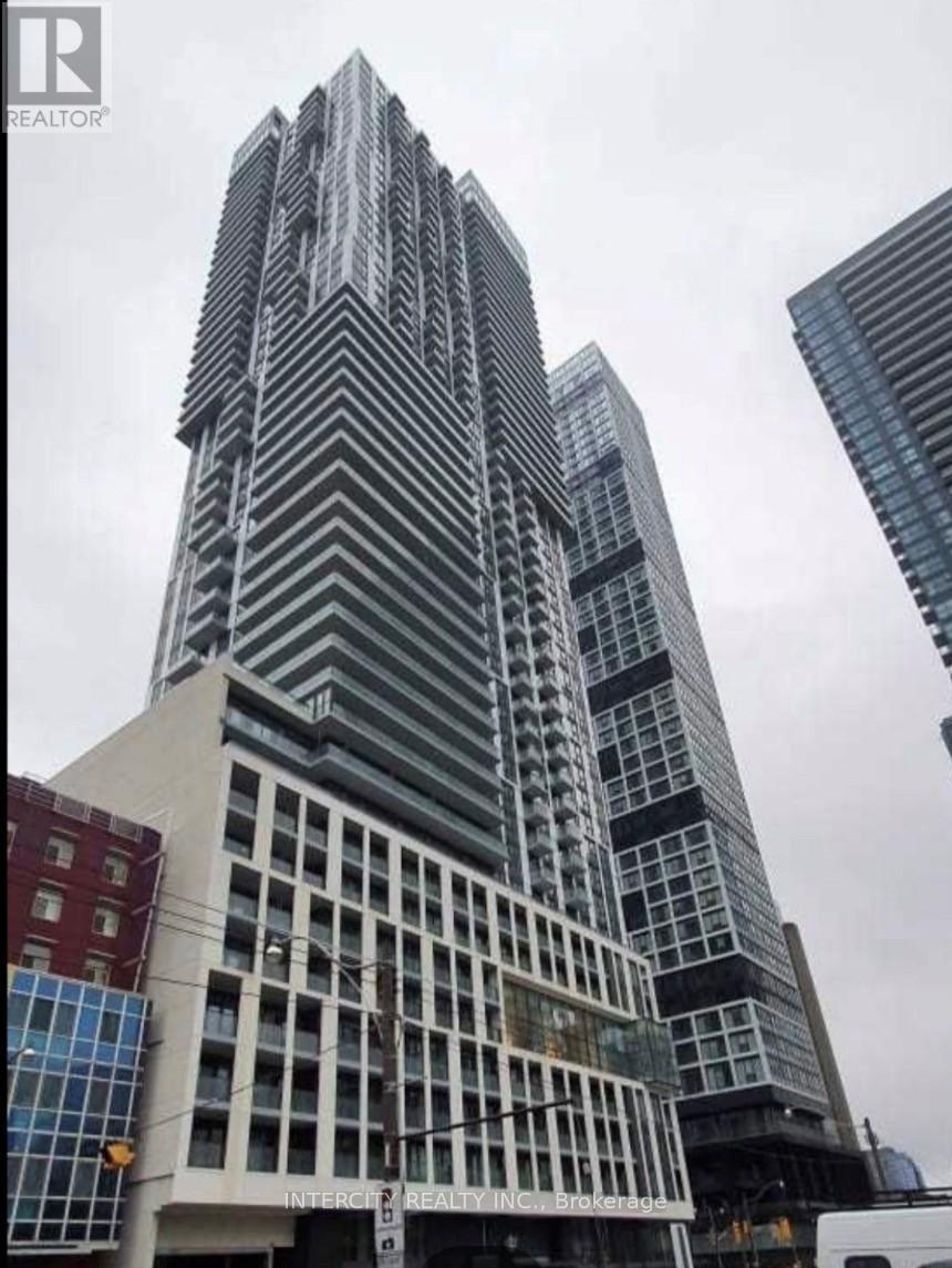A tall building with a glass facade stands in front of other buildings.