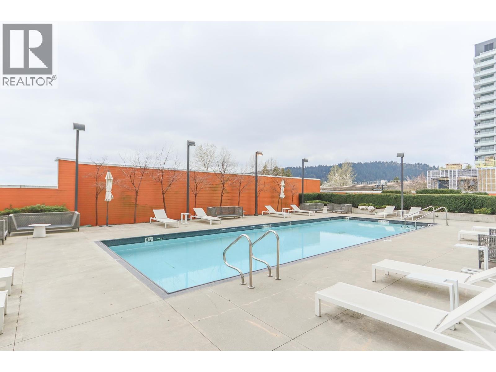A pool with a diving board and lounge chairs.