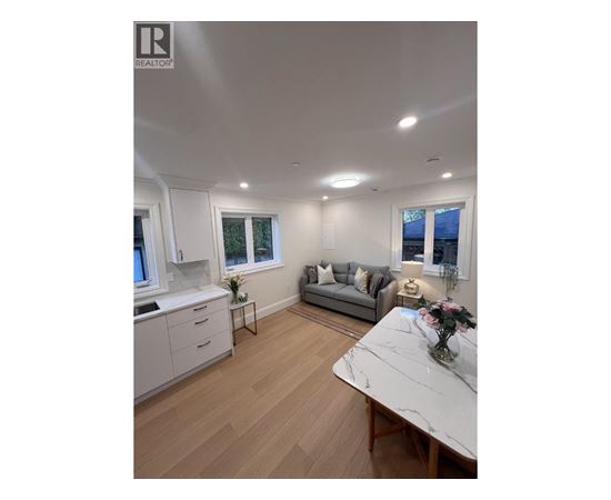 A well-lit, spacious kitchen and living room with a marble table and wooden flooring.
