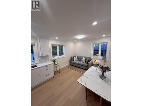 A well-lit, spacious kitchen and living room with a marble table and wooden flooring.