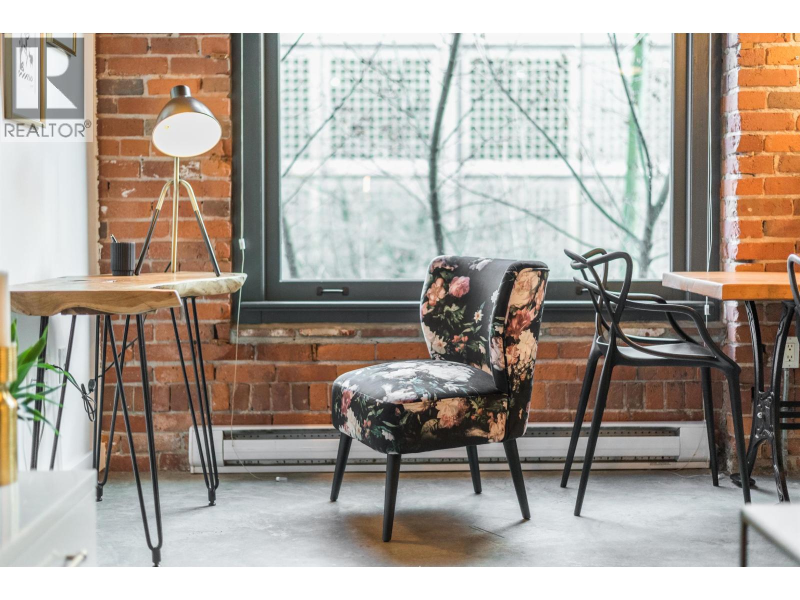A black chair with a floral pattern sits in a room with a brick wall and a window.