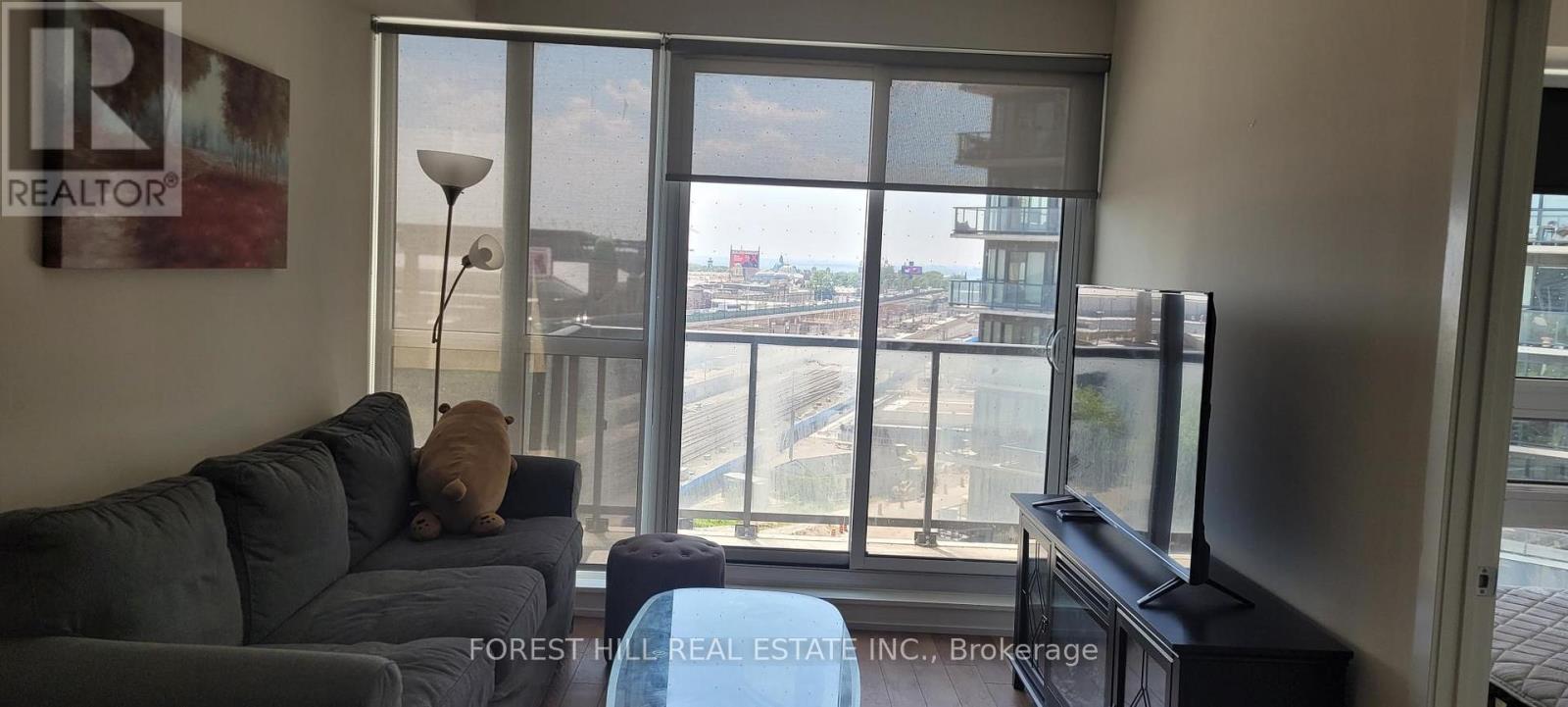A living room with a grey couch and a large window overlooking a parking lot.