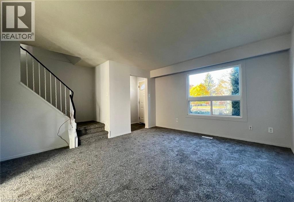 A spacious room with a staircase and a large window showing trees outside.