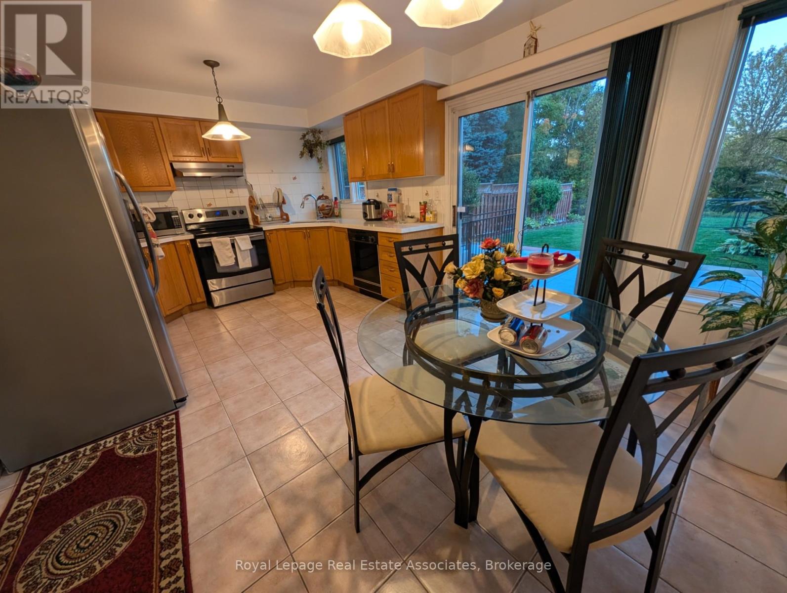 A kitchen with a table and chairs in the foreground and a view of a backyard through the window.