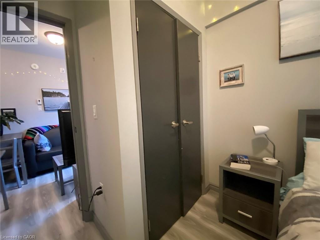 A bedroom with a bed, nightstand, and a door leading to a living room.