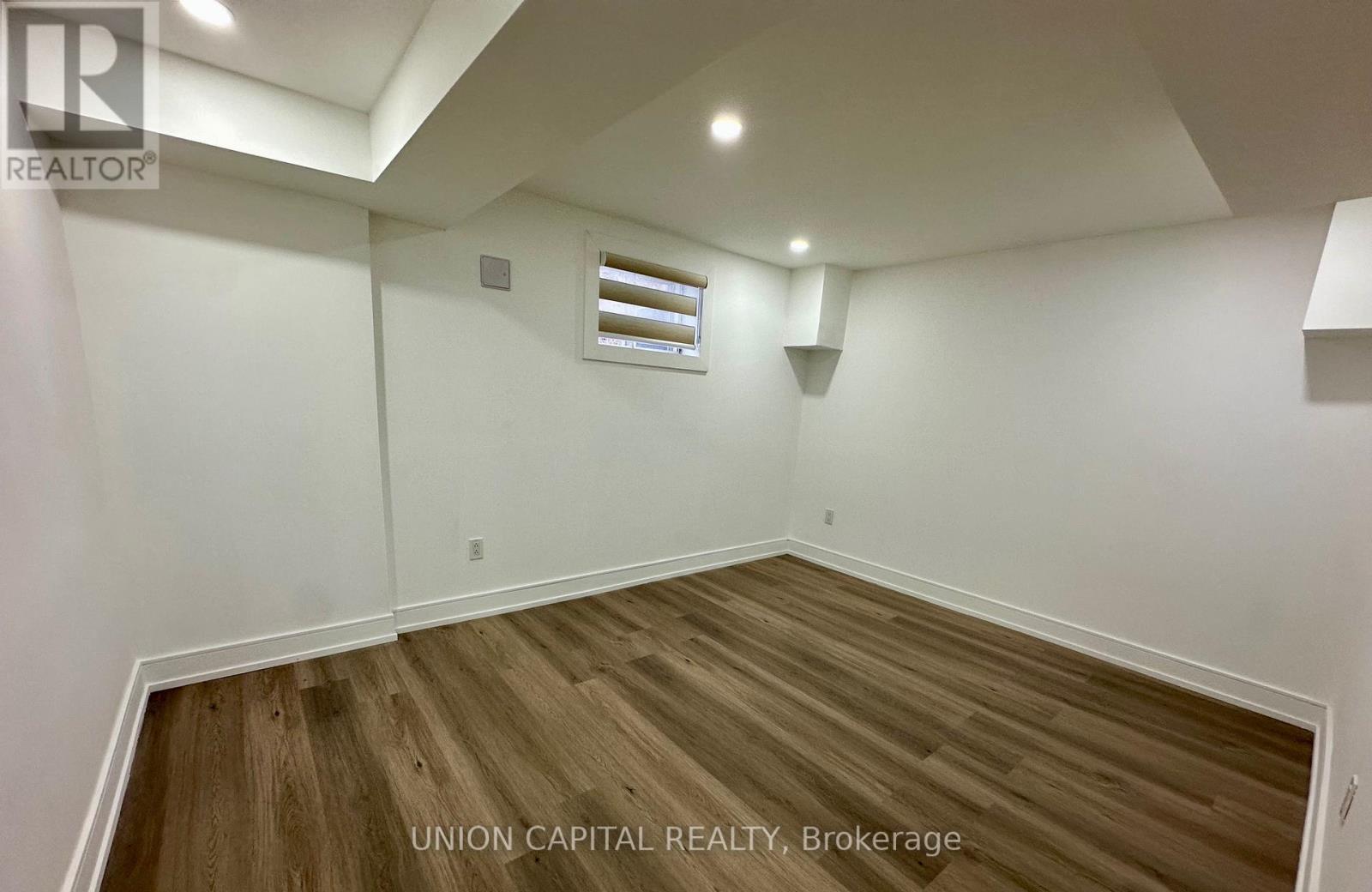 A room with wooden flooring and white walls, with a window and a light fixture on the ceiling.