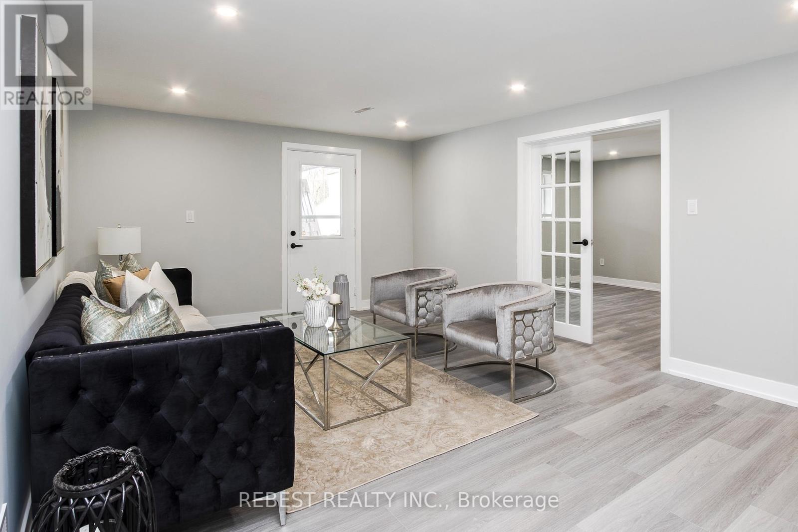 A living room with a black sofa, glass coffee table, and a white door.