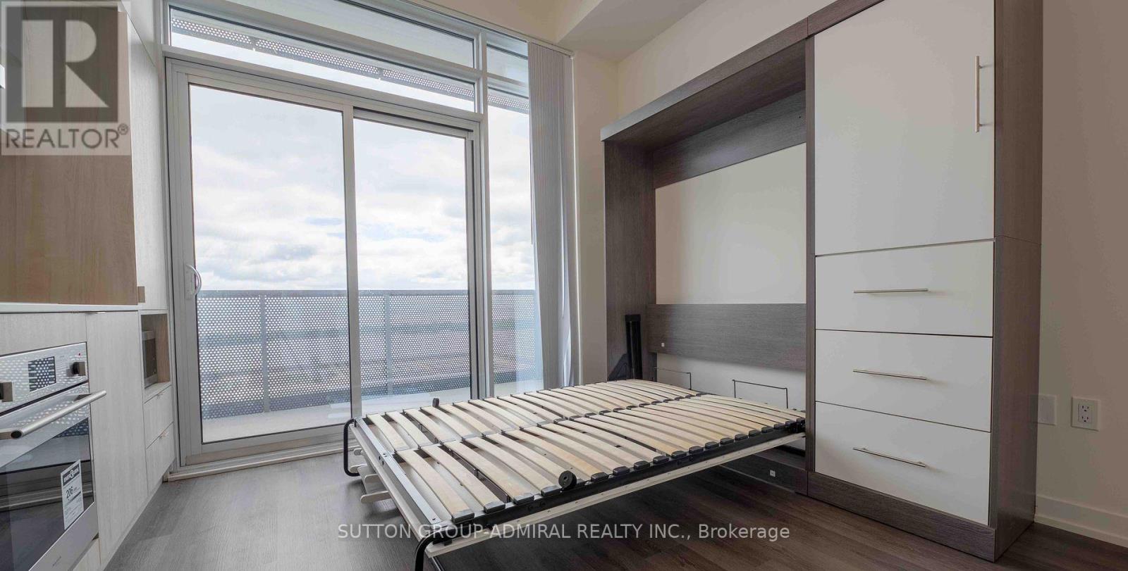 A bedroom with a bed, dresser, and a window overlooking a balcony.