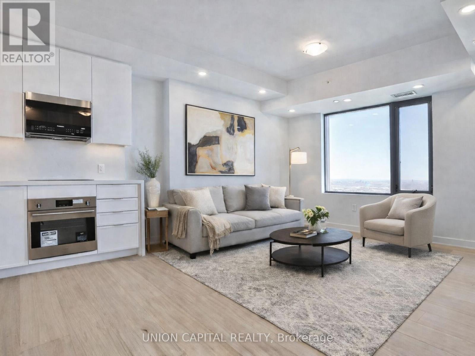A modern living room with a grey rug, a grey sofa, a grey armchair, a coffee table, a television, and a plant.