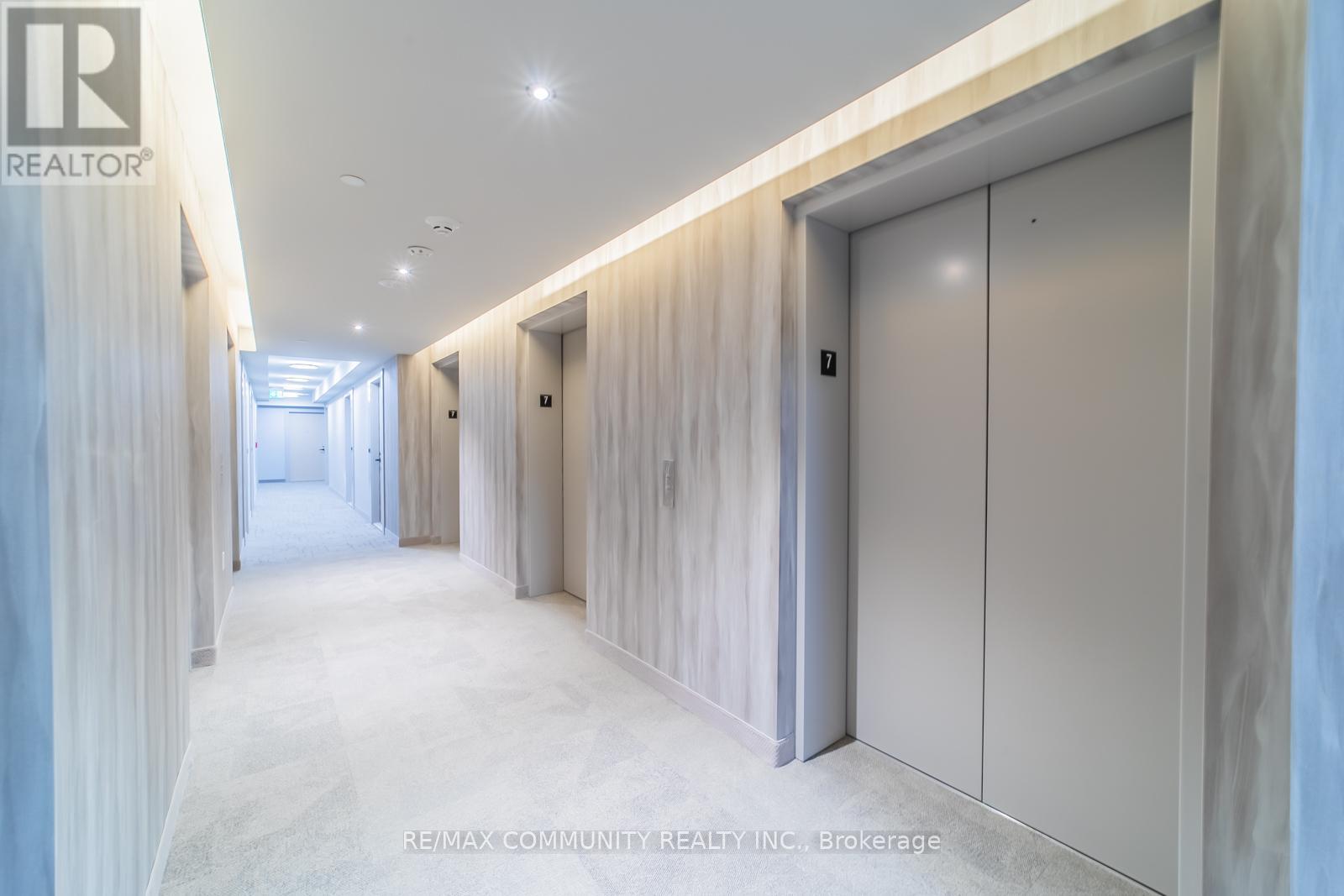 A long hallway with a white floor and walls, and a row of white doors on the right side.
