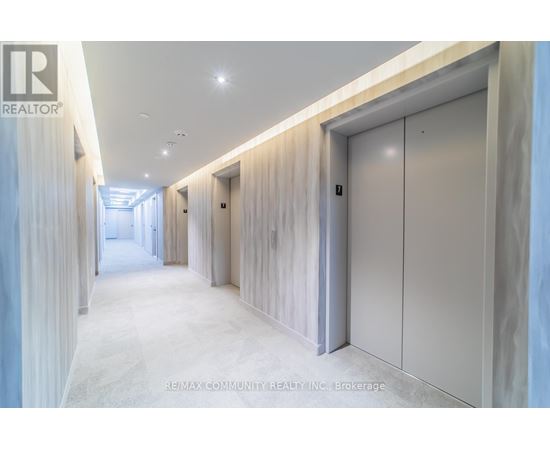 A long hallway with a white floor and walls, and a row of white doors on the right side.