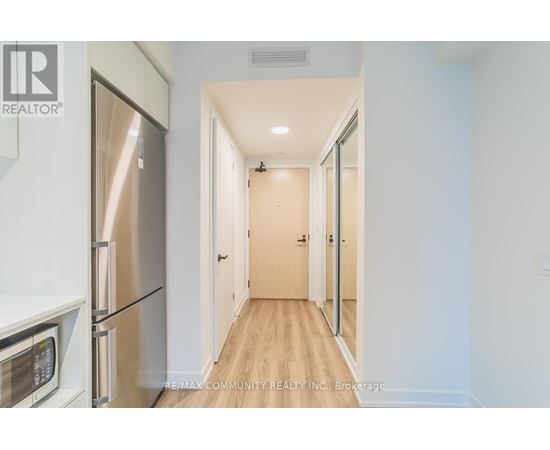 A kitchen with a refrigerator and microwave on the left and a hallway on the right.