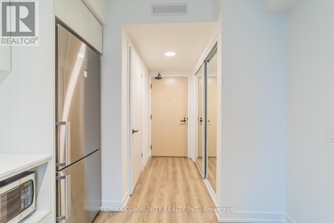 A kitchen with a refrigerator and microwave on the left and a hallway on the right.