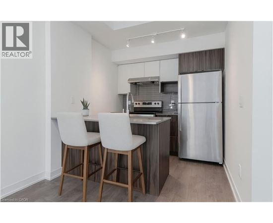A modern kitchen with white chairs and a stainless steel refrigerator.