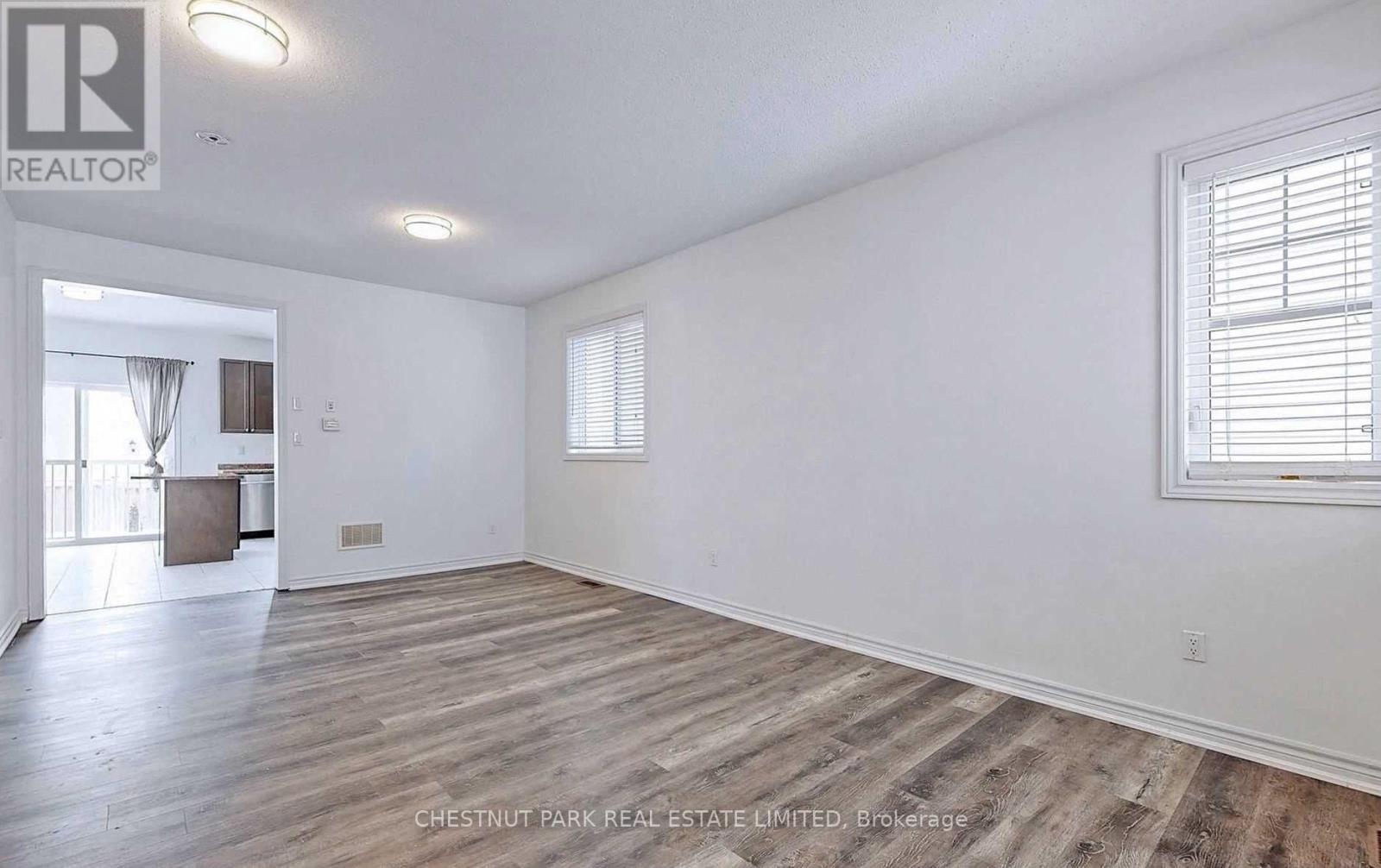 A spacious room with wooden flooring and a window on the right side.