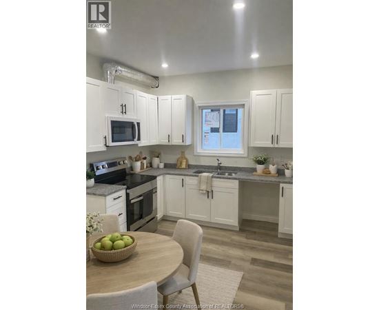A kitchen with white cabinets and a wooden table with a bowl of fruit on it.