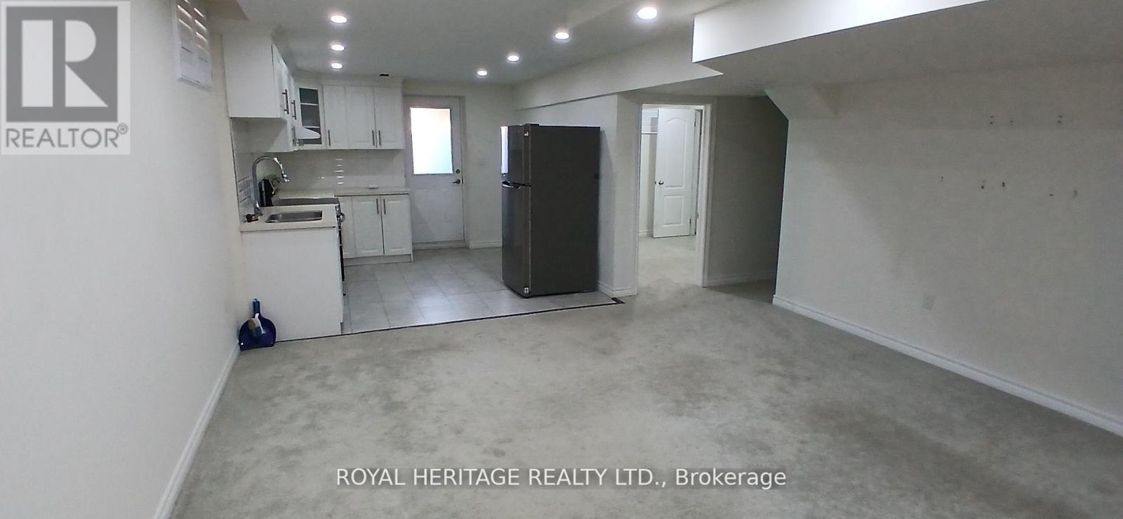 A spacious room with a kitchen area in the background and a refrigerator in the foreground.
