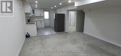 A spacious room with a kitchen area in the background and a refrigerator in the foreground.