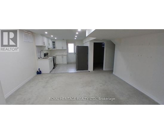 A spacious, empty room with white walls and a kitchen area in the background.