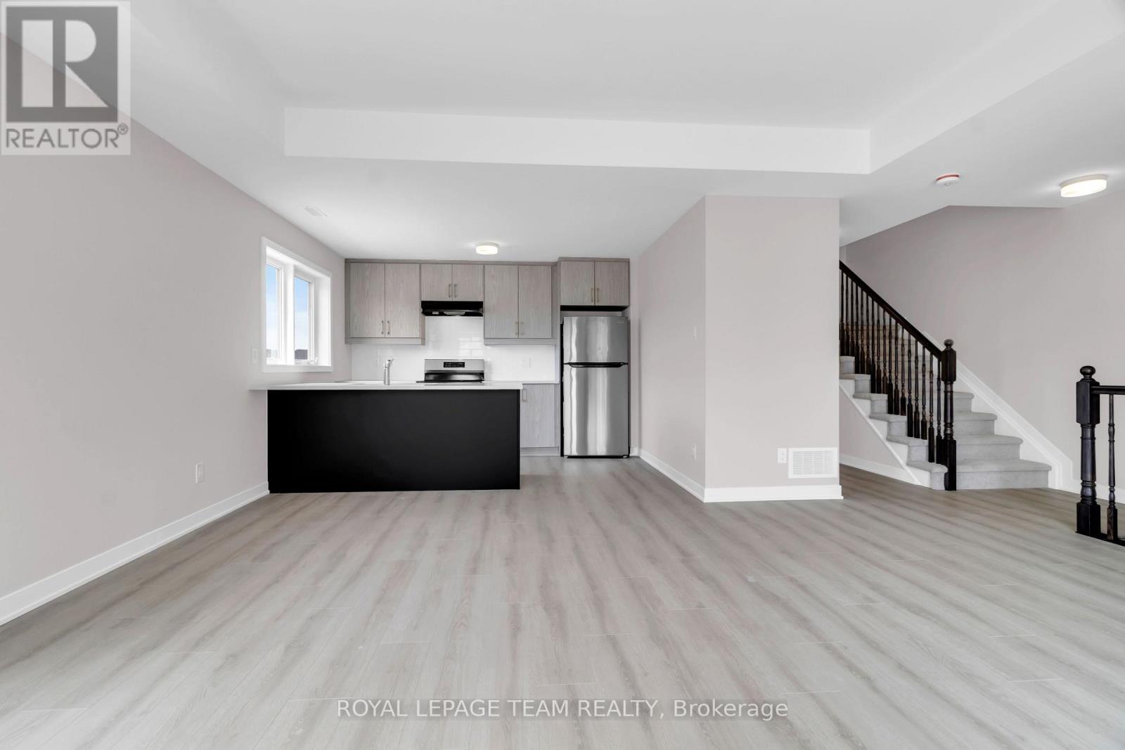 A spacious, well-lit kitchen with a stainless steel refrigerator and a staircase leading to the upper floor.