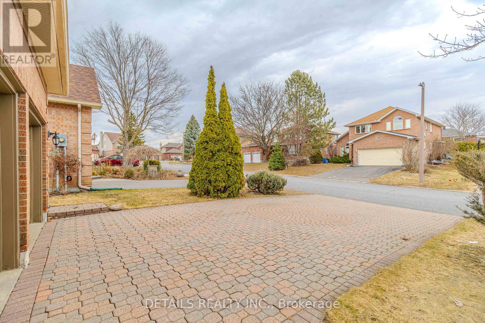 A brick driveway leads to a house with a realtor sign in the foreground.